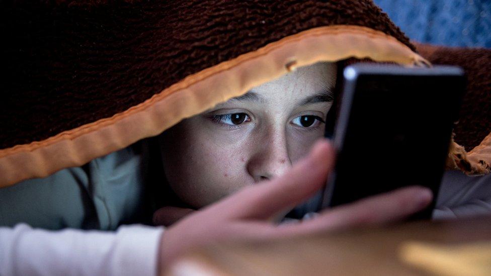 Child looking at a phone in bed