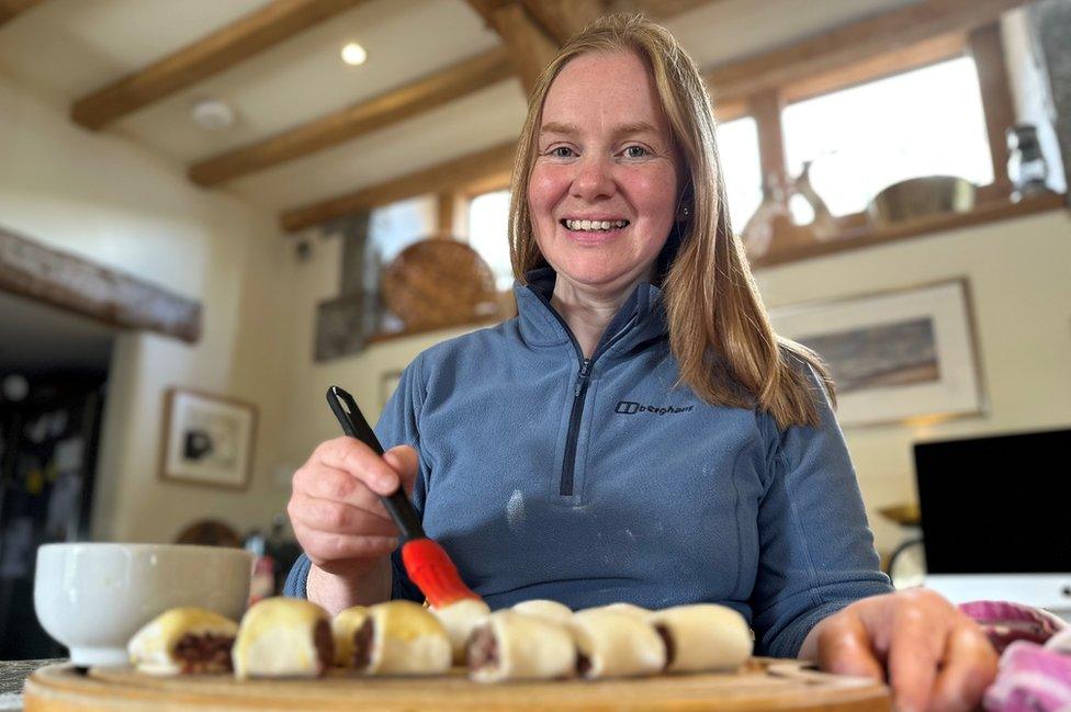 A woman smiles at the camera while brushing sausage rolls