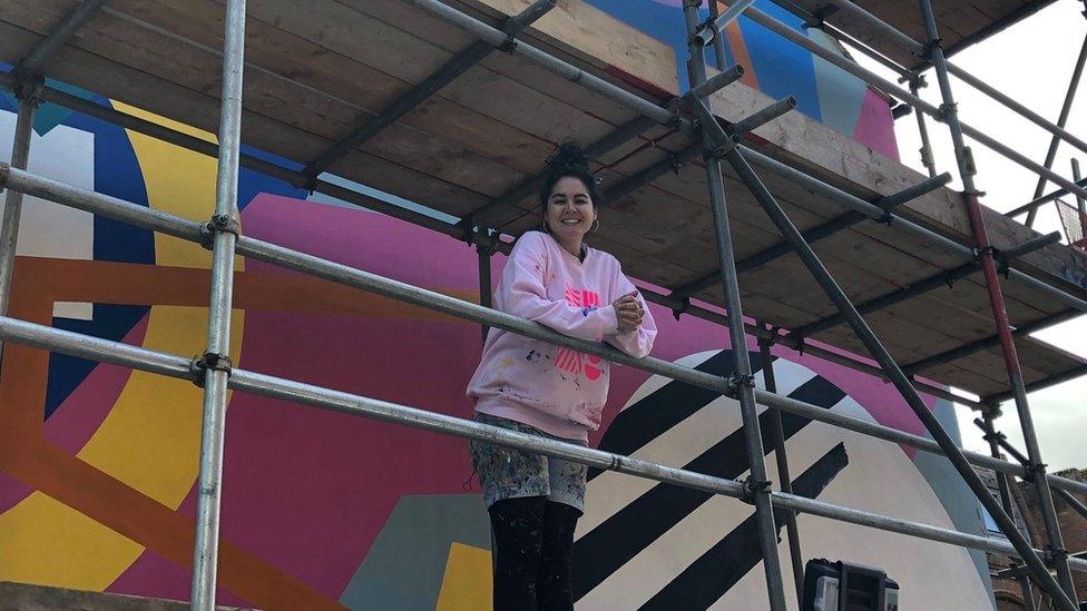 Eloisa Henderson-Figueroa smiling in front of a mural she is painting