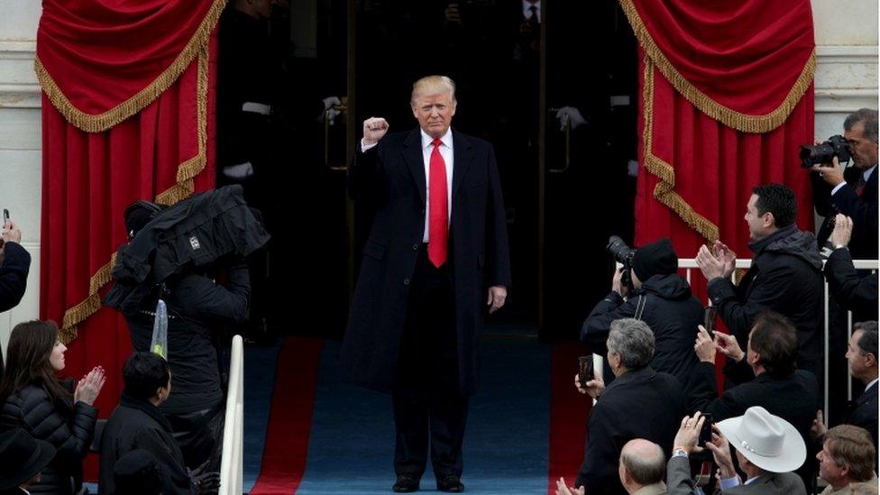 Donald Trump raising a fist, surrounded by cameras, arriving to his inauguration ceremony