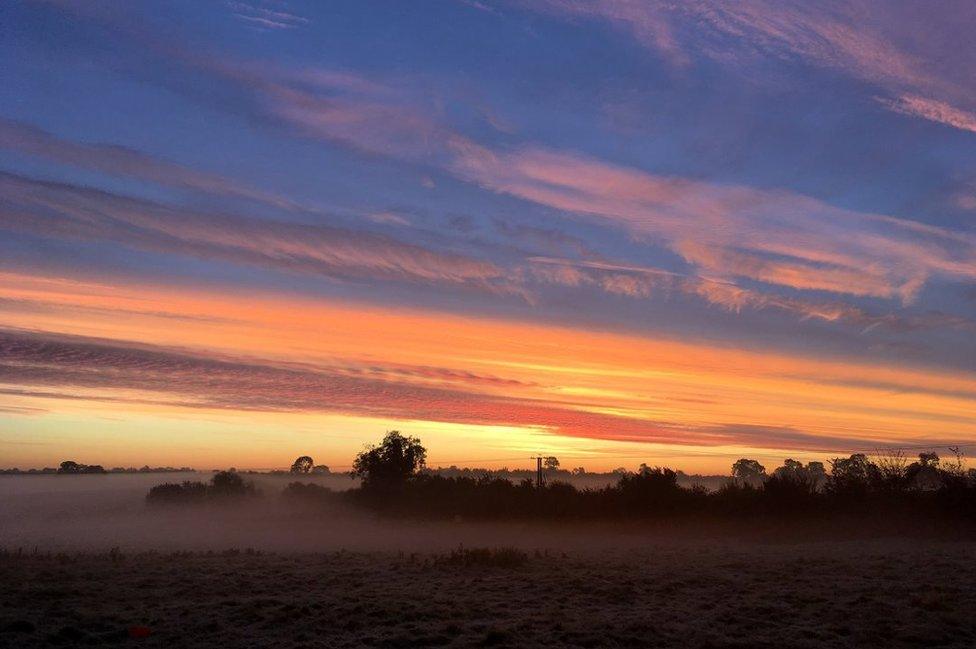 View of sunrise over fields with morning mist