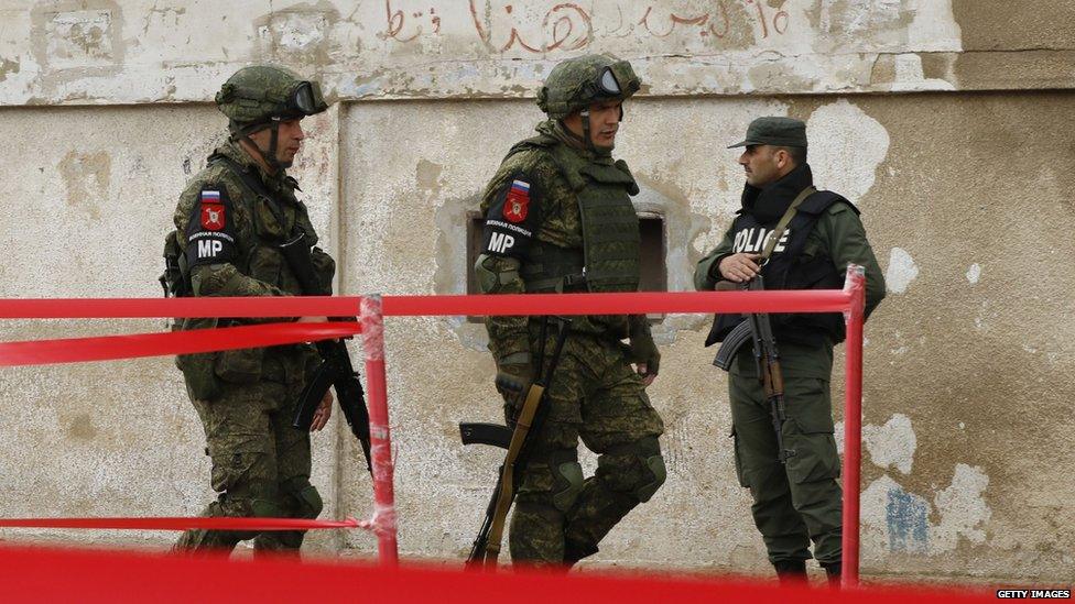 Members of the Russian military police walk past a Syrian regime soldier in Homs, Syria