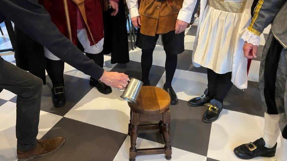 A man pouring ale onto a mahogany stool