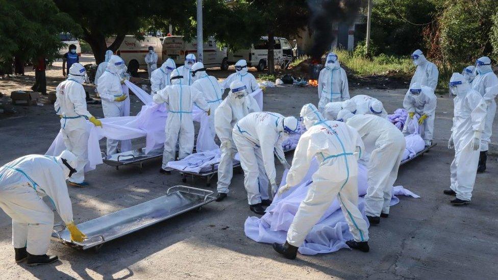 Volunteers wearing personal protective equipment (PPE) arrange bodies of people who died from the Covid-19 coronavirus during their funeral at a cemetery in Mandalay on July 14, 2021.