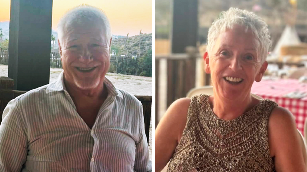 A smiling man and woman sat outside in the sun.