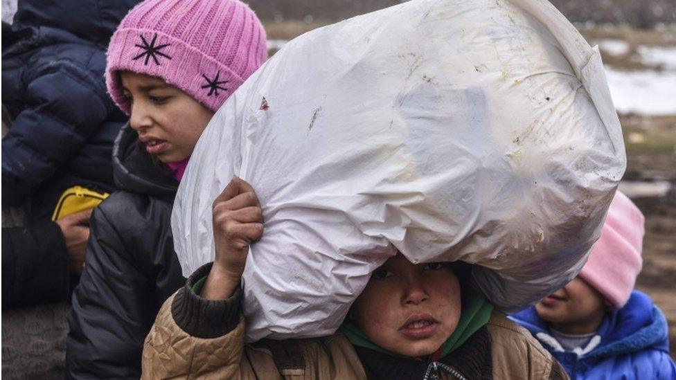 A child migrant holds his belongings as he waits on the Macedonian border into Serbia