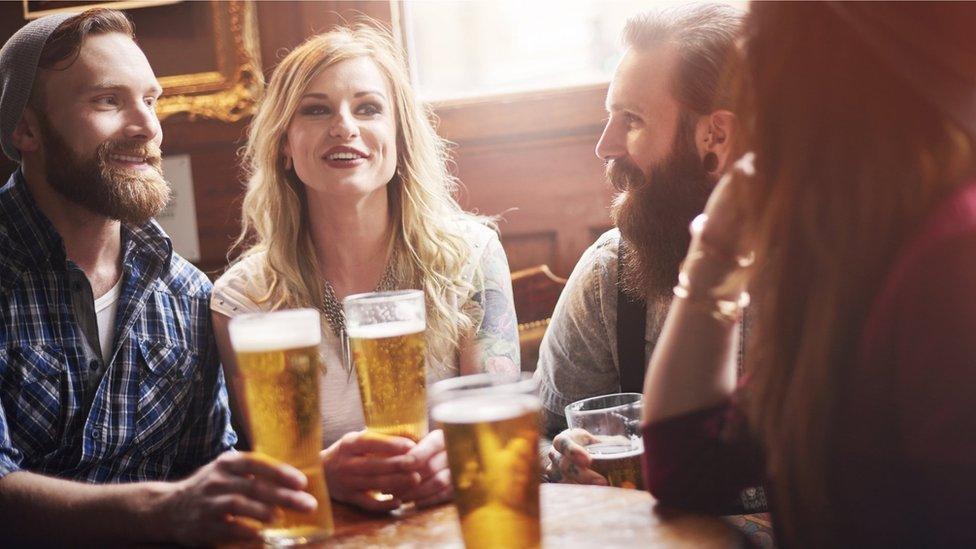 Four friends sitting at a pub table drinking beer