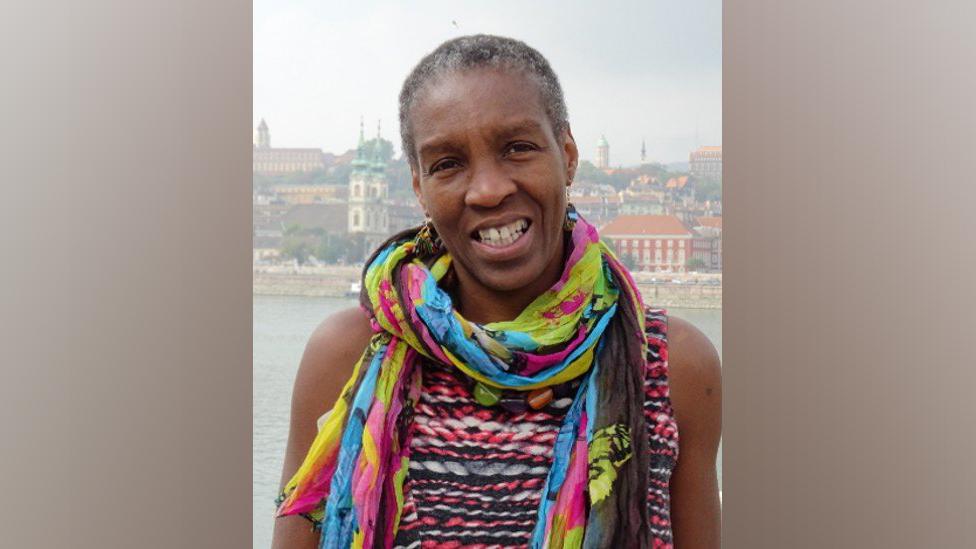 Ruth Pitter wearing a multicoloured scarf and woven top near a river