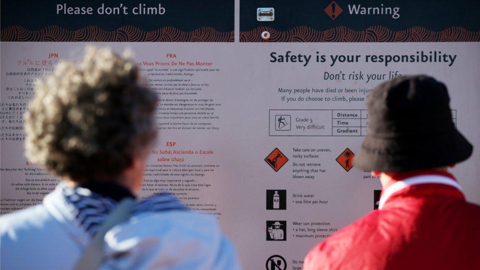 Visitors read the 'please don't climb' and warning signs at the base of Uluru