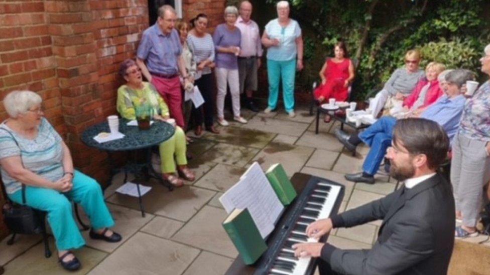 Father Lee Taylor playing the piano to a crowd as his annual garden party, before Covid restrictions came in