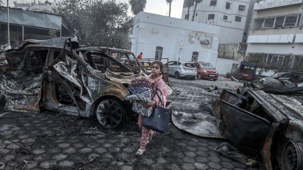 A girl tries to collect usable belongings amid wreckage of vehicles after Al-Ahli Baptist Hospital