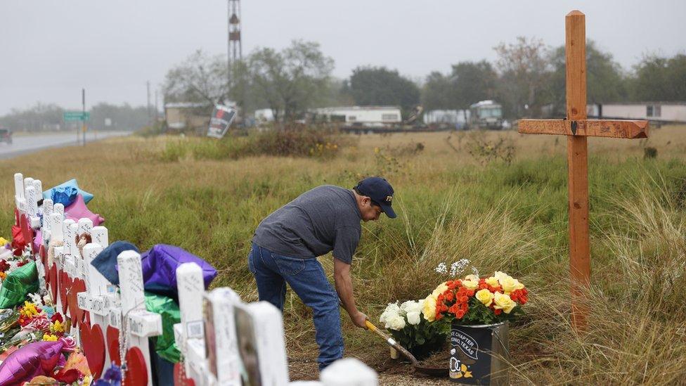 San Antonio resident, Rey Flores digs up sand to place flowers next to a cross left for a memorial to the 26 people who died