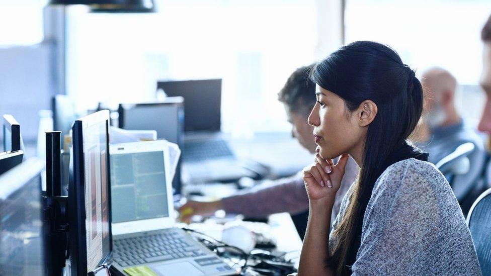 Woman sits at a desk filled with computers