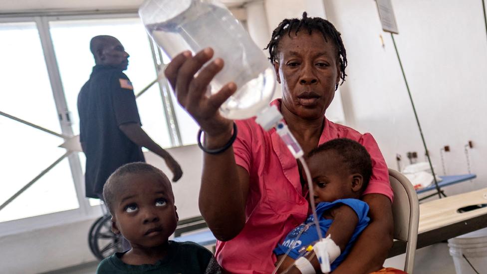 Etienne Lionesse holds an IV solution bag for her son as he receives treatment for cholera