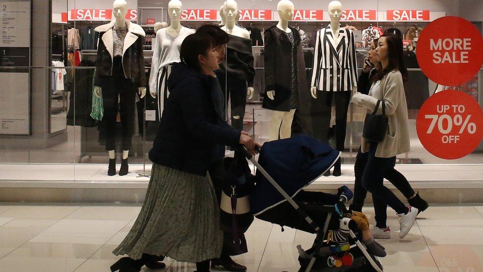 Shoppers walk past sales signs in Tokyo