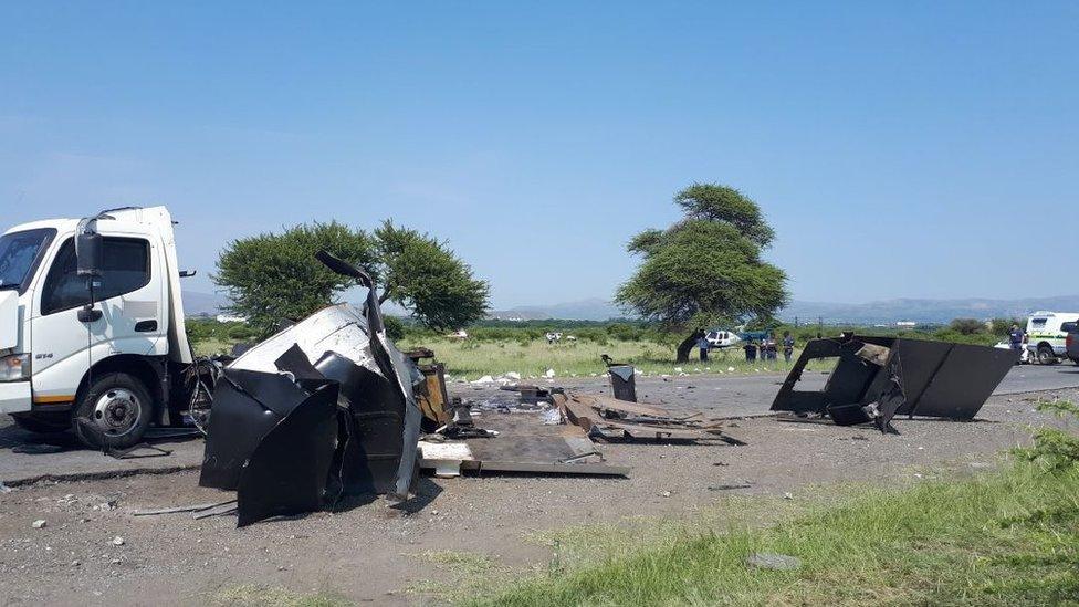 A destroyed van with police and a helicopter in the background