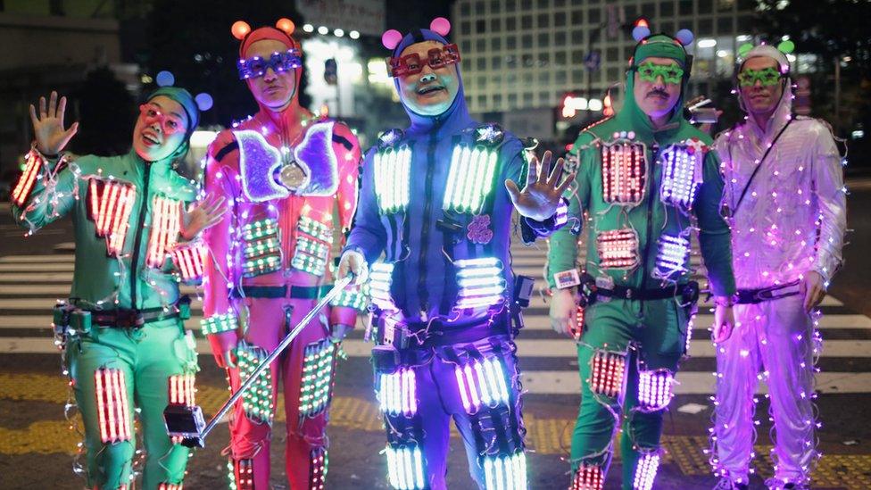 People dressed in bright neon suits covered in lights.