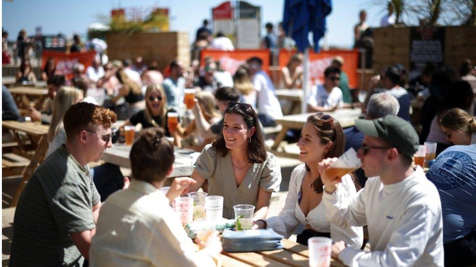 People sit at an outdoor bar as they enjoy the hot weather on Brighton pier, in Brighton