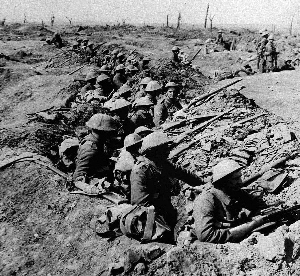 British infantrymen occupying a shallow trench in a ruined landscape before an advance during the Battle of the Somme