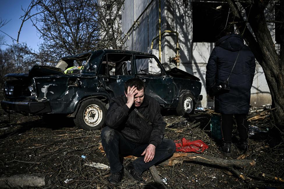 A man sits outside his destroyed building after bombings on the eastern Ukraine town of Chuhuiv on 24 February 2022