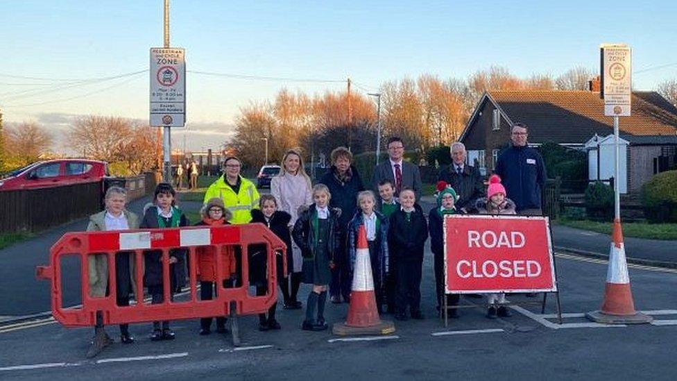 Pupils and school staff standing by barriers at the end of a school road