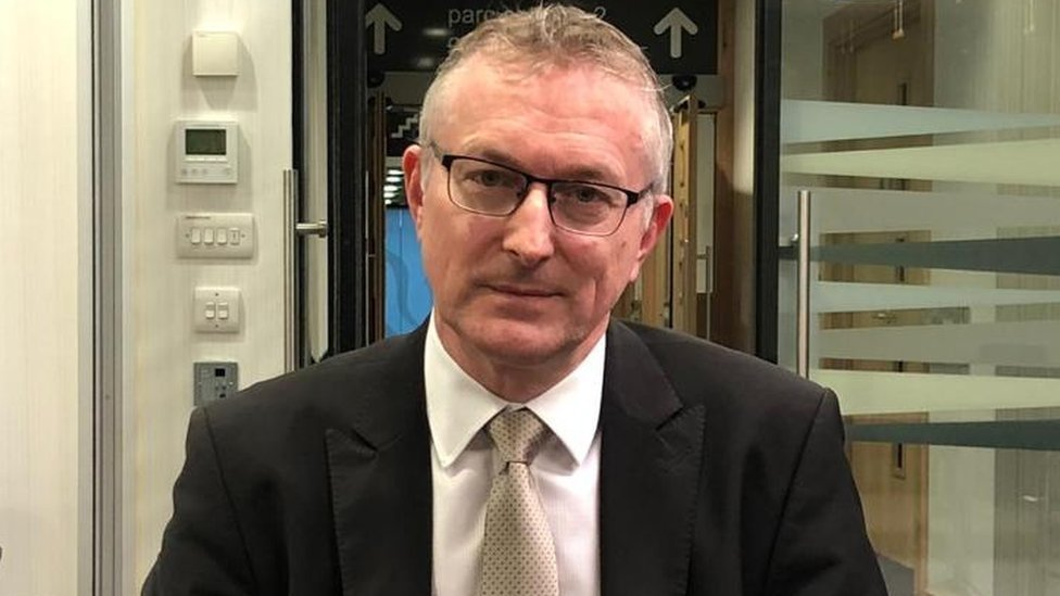 Andrew Goodall, head of the civil service in Wales, wearing a dark suit and light tie, looking straight into the camera in a room