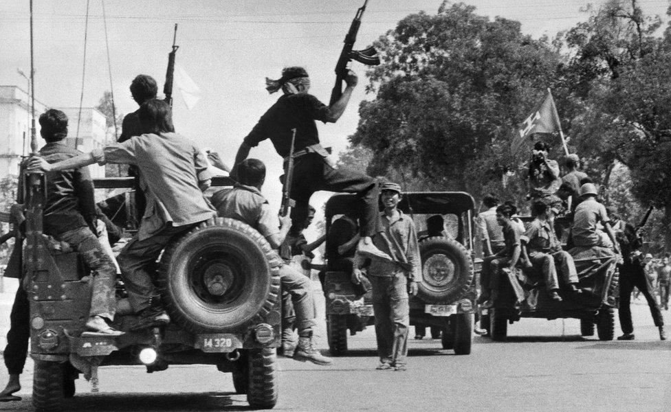 The Khmer Rouge guerilla soldiers wearing black uniforms (C), drive 17 April 1975 atop jeeps