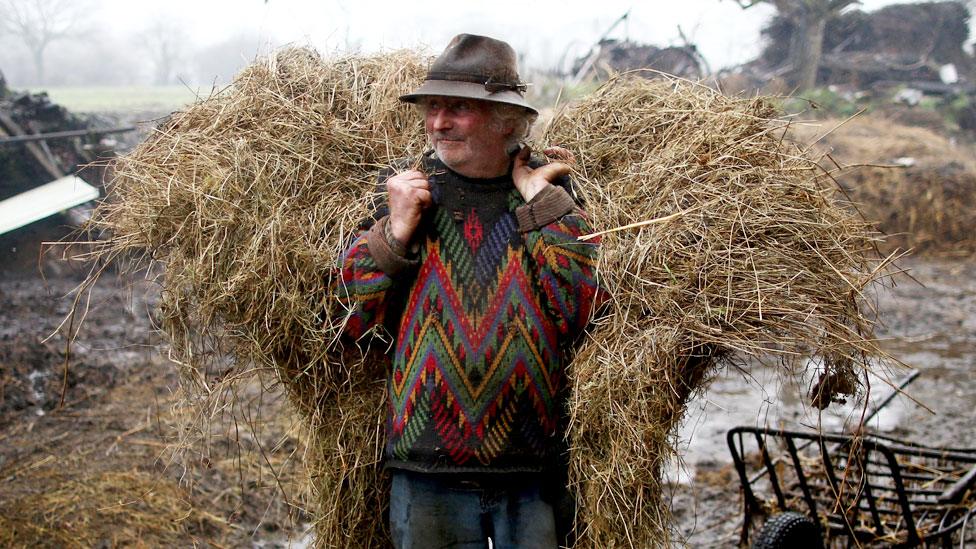 Farmer Jean-Bernard Huon stands on his farm with a bail of hay on his back.