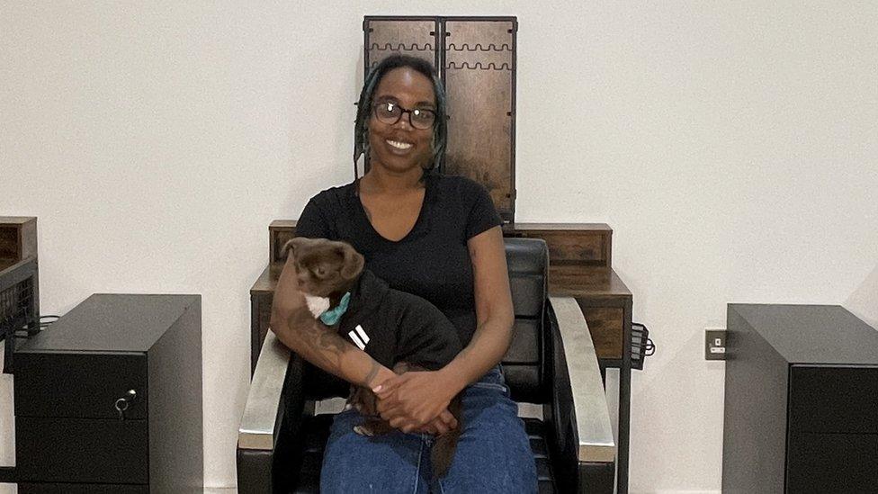 A woman sat on a salon chair with a dog on her lap