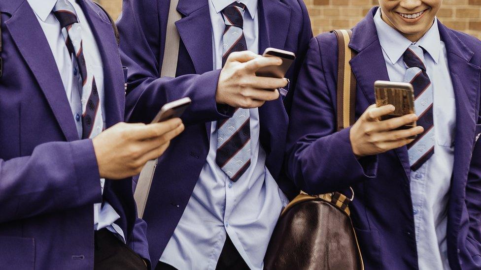 Three school pupils look at their mobile phones