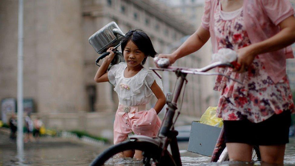 A little girl carrying two kettles walks around waterlogged street on July 20, 2016 in Tianjin, China. Heavy rains hit Tianjin, disrupting traffic in the Chinese capital.