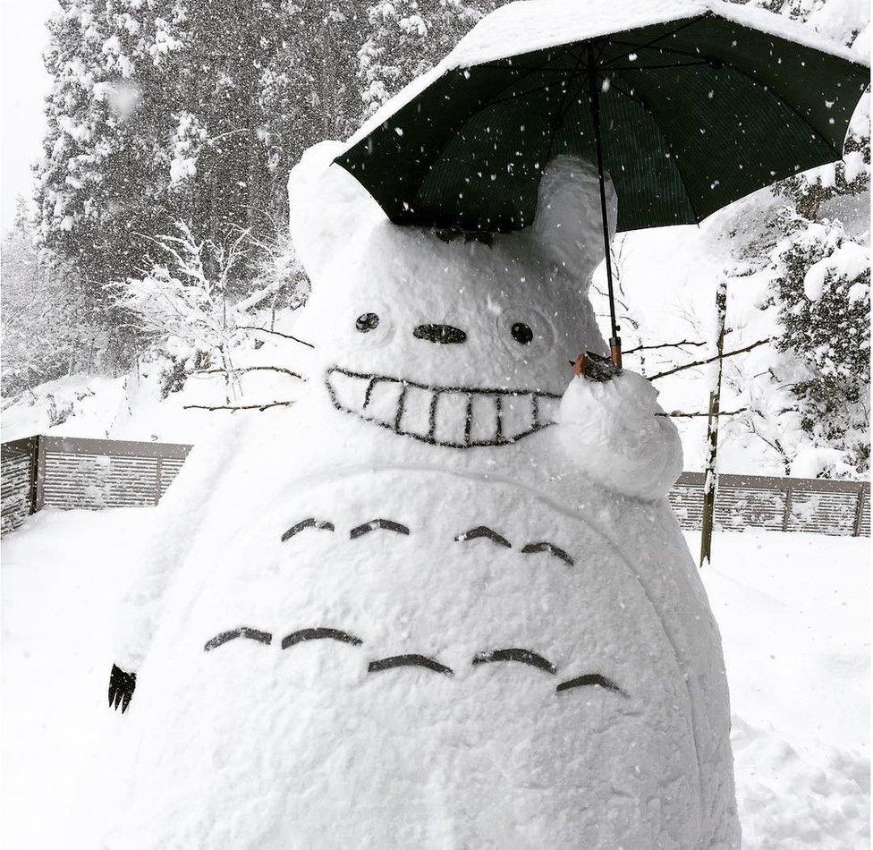 A Totoro made of snow, carrying an umbrella.