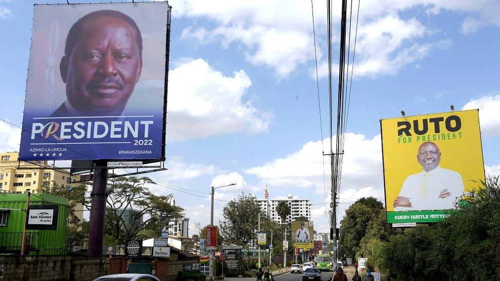 Pedestrians and motorists are seen next to campaign posters for Presidential candidates for Azimio La Umoja (Aspiration to Unite) Raila Odinga (L) and United Democratic Alliance (UDA) William Ruto, in Nairobi on June 30, 2022