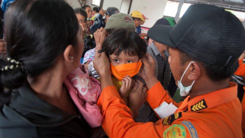 An officer with the disaster management agency BPBD places a mask on child at a shelter