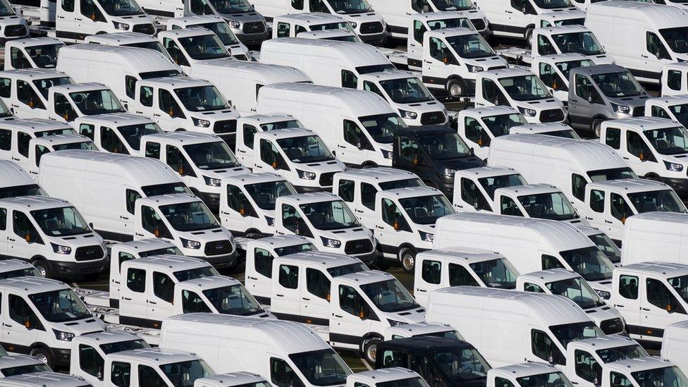 A photograph shows hundreds of white vans parked in neat lines queuing in a port. There are two non-white vans visible - one black and one grey