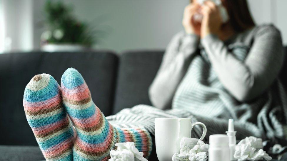 A woman off sick with a tissue to her nose