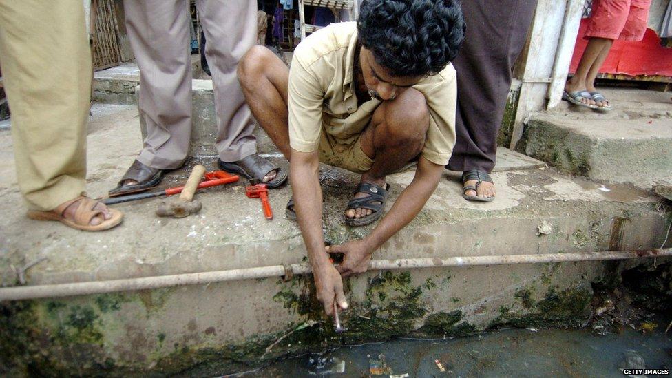 An Indian worker from the Brihanmumbai Muncipal Corporation (BMC) worker is watched by bystanders as he makes repairs on a drinking waterpipe that runs through sewage waste in a slum district in Mumbai