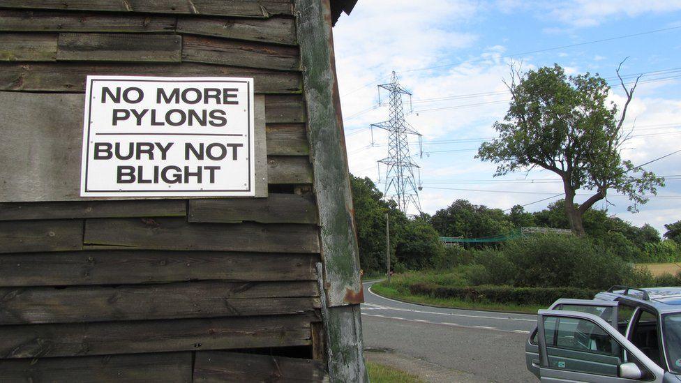 Pylons in East Anglia in the background to a protest sign on the side of a wooden barn.