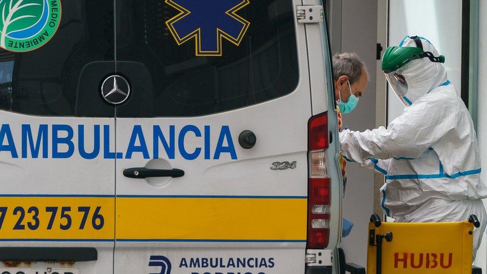 A health worker in a protective suit helps a man come out of an ambulance outside the Burgos Hospital in northern Spain on March 23, 2020