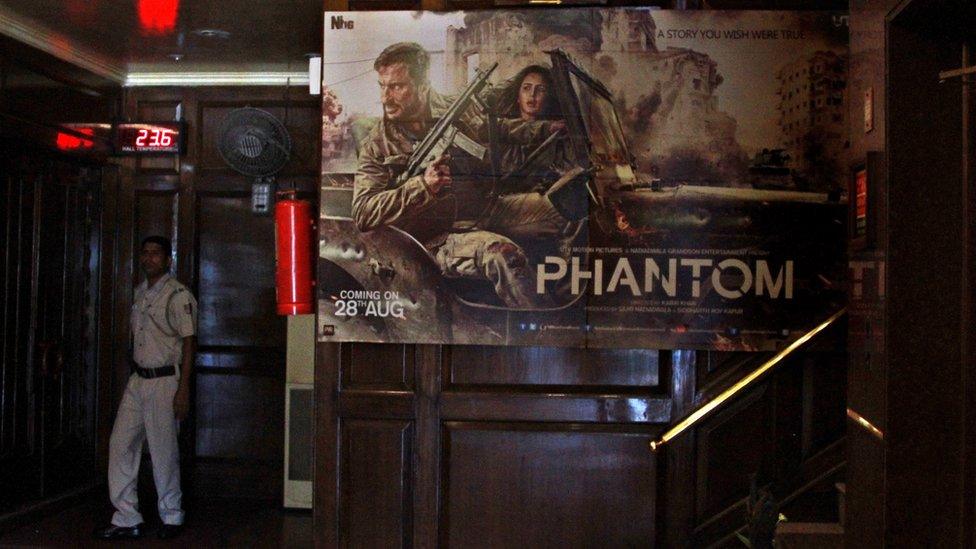 An Indian security guard stands near a poster of upcoming Bollywood movie "Phantom", scheduled to release in India on Aug. 28, at a multiplex in New Delhi, India, Friday, Aug. 21, 2015.