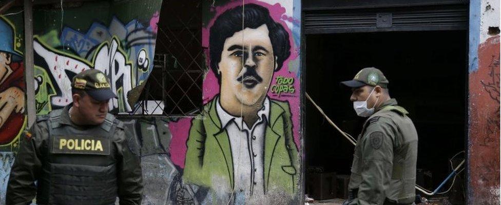 Police officers stand in front of a mural depicting the late drug kingpin Pablo Escobar, in the area known as El Bronx in downtown Bogota, Colombia, Monday, May 30, 2016.