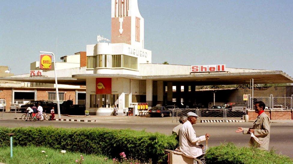 The garage in use, with Shell petrol station signs outside and people standing talking