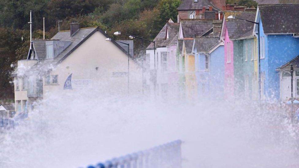 Waves crash onto the promenade in Whitehead, where colourful houses can be seen in the background