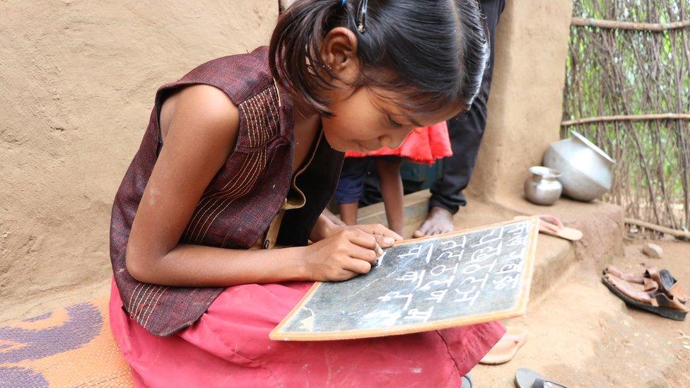 Radhika writing the Hindi alphabet on a slate.