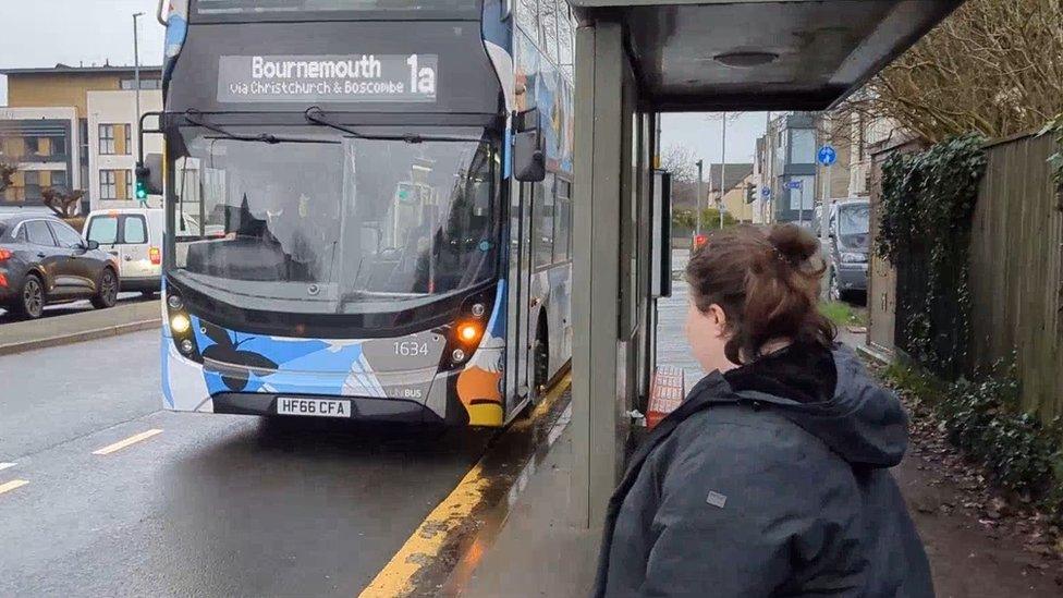 A woman waiting at a bus stop as a bus approaches