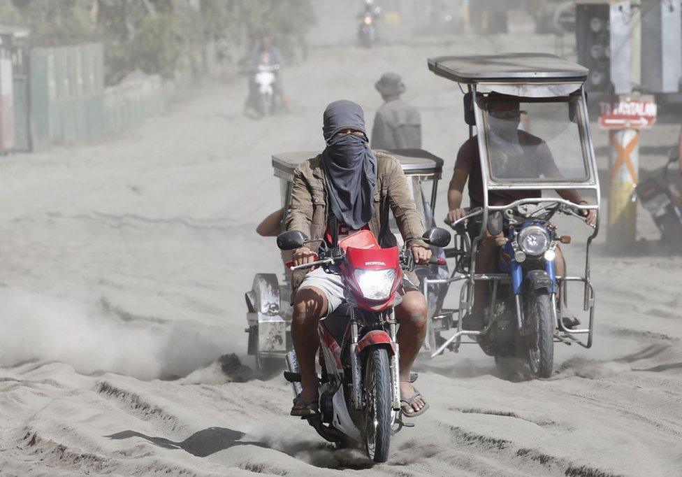 People travel along a road covered in ash deposits, a day after the eruption of Taal Volcano, in Agoncillo town in Batangas province, Philippines, 13 January 2020