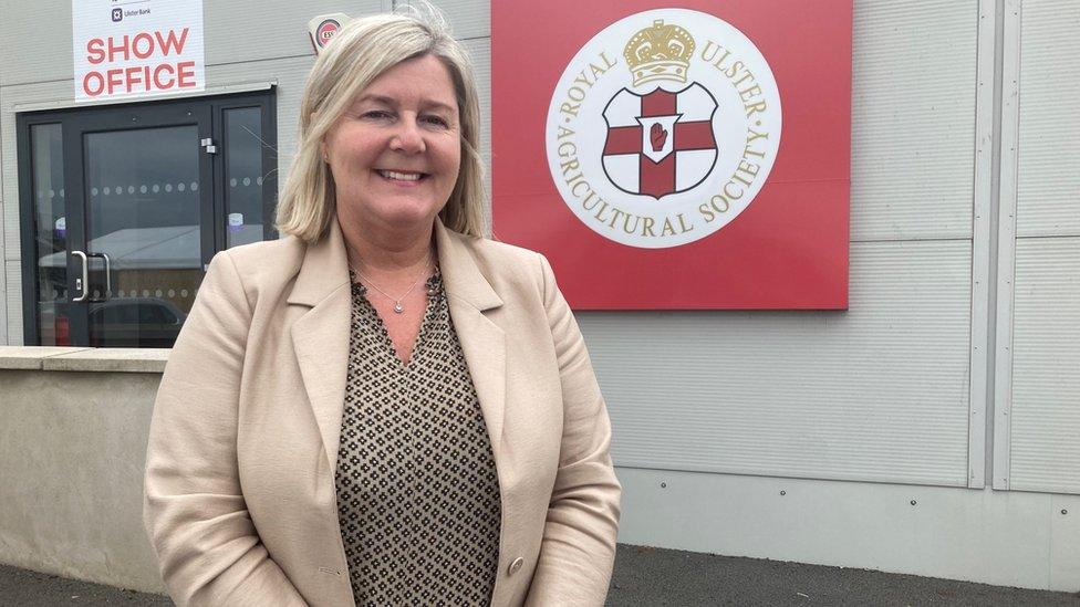 Balmoral Show organiser Rhonda Geary smiles in front of a sign that reads: Royal Ulster Agricultural Society