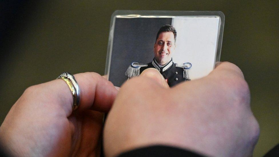 The police officer's widow holds a photo of her late husband in court