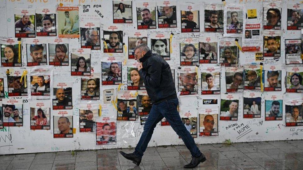 A man walking past a wall adorned with hostage posters in Tel Aviv