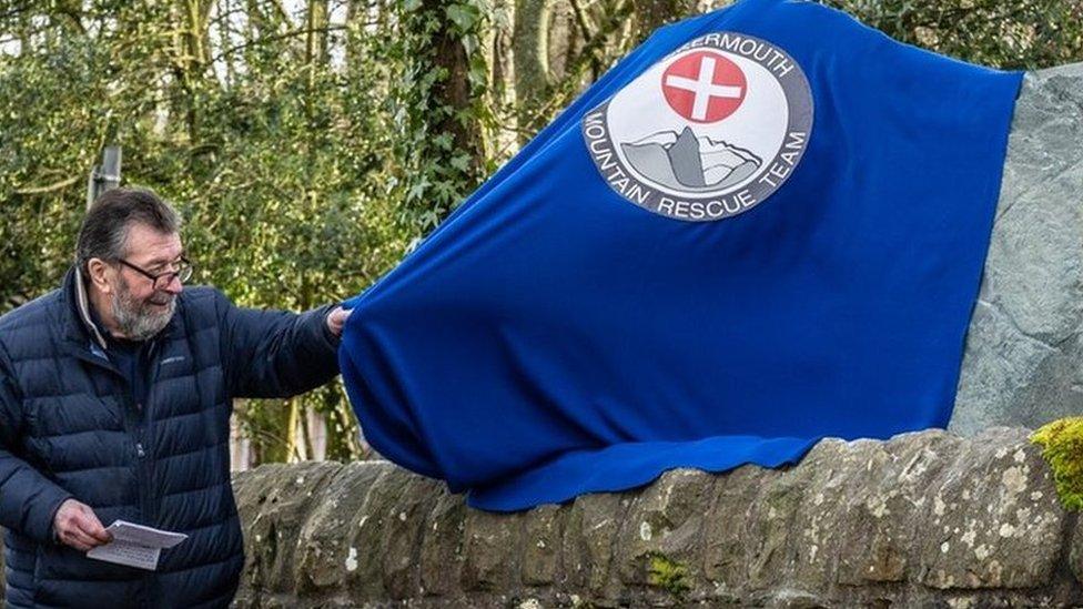 A man pulls a blue cloth away to reveal a large stone sign